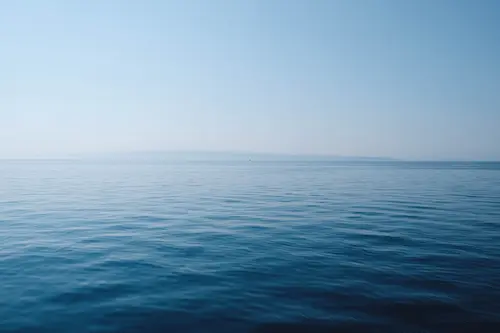 Photo taken out in an ocean in the morning with small waves and a blue and pink sky